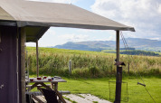 Udsigt over de walisiske bakker fra et telt på Feather Down Pant y March Farm med picnicbord og grønne marker.