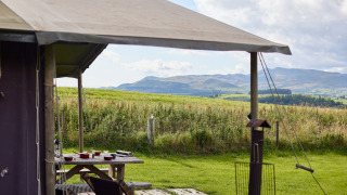 View from a tent at Feather Down Pant y March Farm, Wales, showing a picnic table and rolling hills.