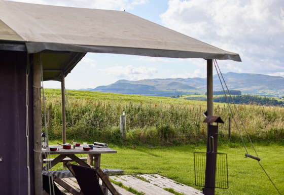 View from a tent at Feather Down Pant y March Farm, Wales, showing a picnic table and rolling hills.