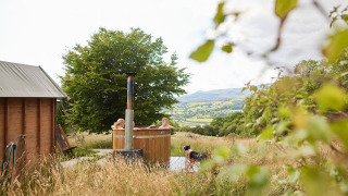 Personas relajándose en una tina de madera al aire libre con vistas al paisaje galés en Feather Down Pant y March Farm.