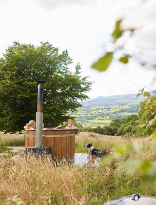 Folk slapper af i et udendørs vildmarksbad med udsigt over det walisiske landskab på Feather Down Pant y March Farm.