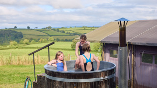Niños se divierten en un jacuzzi exterior en Feather Down Billingsmoor Farm con campos al fondo.