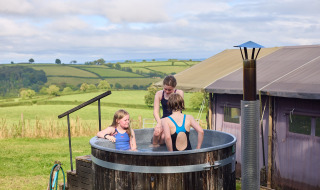 Niños se divierten en un jacuzzi exterior en Feather Down Billingsmoor Farm con campos al fondo.