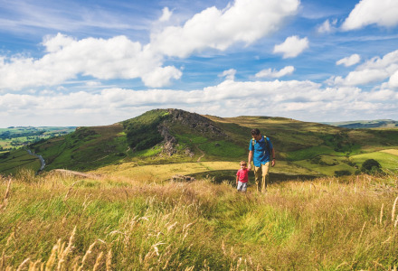 Un hombre y un niño pequeño caminan por colinas verdes cerca de Butterleigh, suroeste de Inglaterra, bajo el cielo azul.