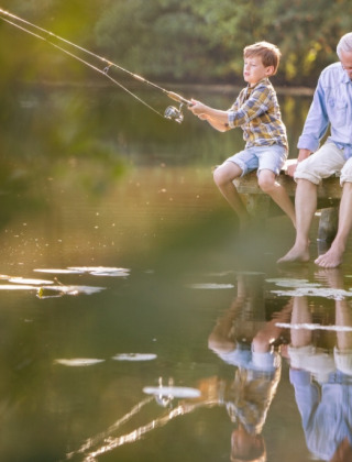Un hombre mayor y dos niños disfrutan pescando juntos en un muelle de madera sobre un tranquilo lago natural.