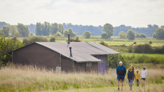 Famille marchant dans une prairie près d'une tente à Feather Down College Farm, parc de vacances en Angleterre.
