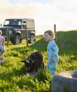 Børn i pyjamas leger på en grøn mark med en ged ved Feather Down Treganhoe Farm i Sydvestengland.