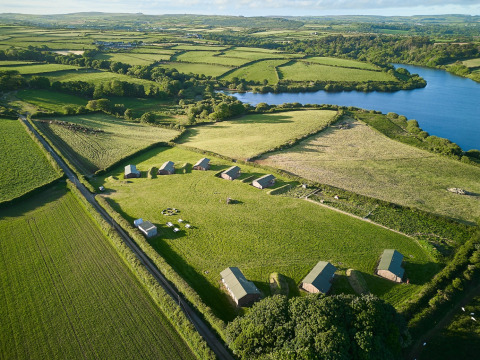 Luchtbeeld van Feather Down Treganhoe Farm, een vakantiedomein omringd door velden en een meer in Zuidwest-Engeland.