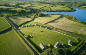 Vista aerea di Feather Down Treganhoe Farm, parco vacanze circondato da campi verdi e un lago nel sud-ovest inglese.