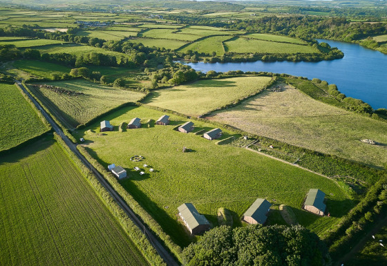 Luftfoto af Feather Down Treganhoe Farm, et feriecenter omgivet af marker og en sø i det sydvestlige England.