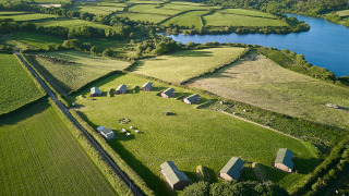 Aerial view of Feather Down Treganhoe Farm holiday park, surrounded by lush fields and a lake in southwest England.