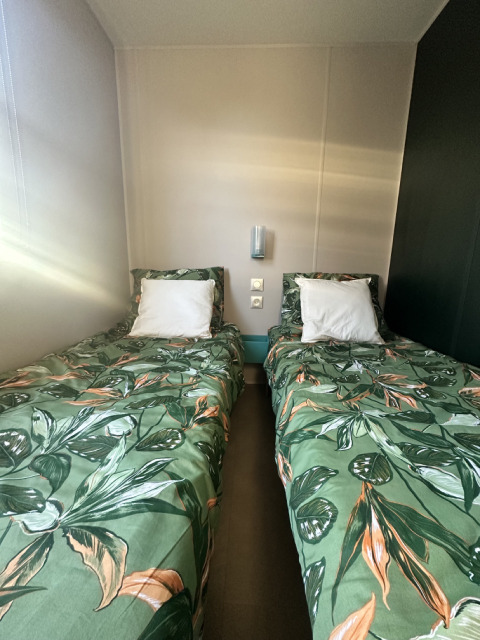 Twee eenpersoonsbedden met groene bladmotief hoeslakens in een lichte en moderne glamping kamer.