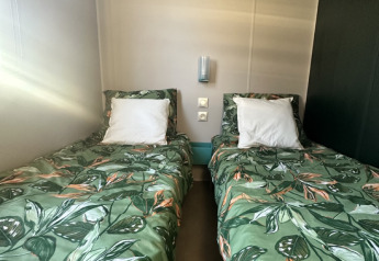 Zwei Einzelbetten mit grüner Blatt-Bettwäsche in einer Glamping-Unterkunft mit schlichtem Design.