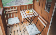 Petite terrasse d’une cabane Gipsy wagon avec deux chaises, table et vue sur l’espace vert.