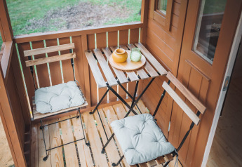Petite terrasse d’une cabane Gipsy wagon avec deux chaises, table et vue sur l’espace vert.