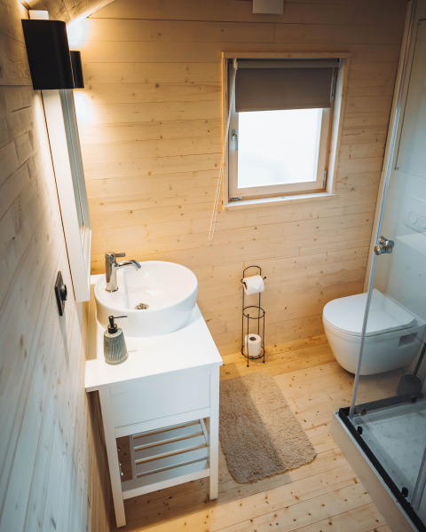 Helles Badezimmer aus Holz in einer Hütte mit Waschbecken, Toilette und Dusche im Camping Papillon, Belgien.
