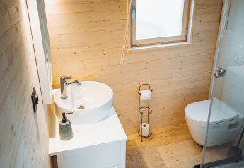 Bagno in legno chiaro in una cabina con lavabo, WC e doccia al Camping Papillon in Belgio.
