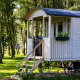 Cabaña de carro gitano con terraza en bosque soleado, rodeada de árboles y césped natural verde.