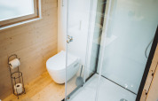 Baño contemporáneo en cabaña de madera con ducha acristalada, inodoro suspendido y ventana amplia.