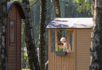 Iemand zit op het terras van een Gipsy wagon op Camping Papillon in België, omgeven door bomen.