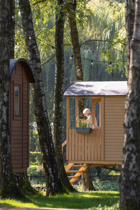 A person sits on the terrace of the Gipsy wagon cabin surrounded by trees at Camping Papillon, Belgium.