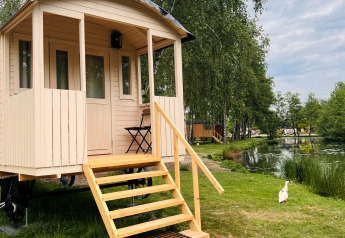Gipsy wagon med terrasse ved Camping Papillon i Belgien, placeret ved en sø omgivet af træer.