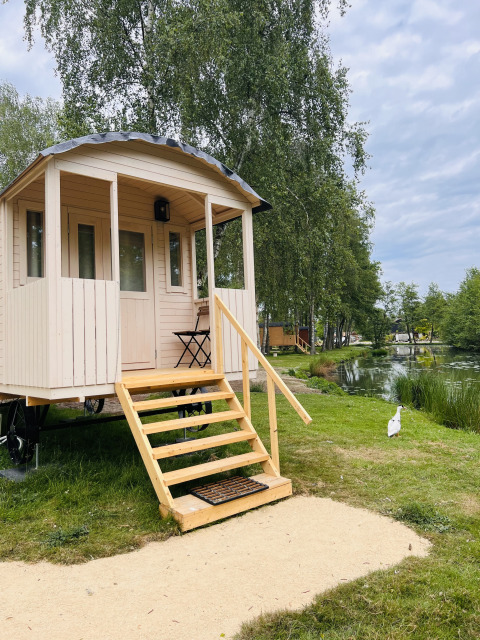 Gipsy wagon with terrace at Camping Papillon in Belgium, situated by a pond and surrounded by trees.