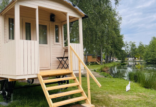Roulotte avec terrasse au Camping Papillon en Belgique, près d’un étang et entourée d’arbres.