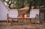 Coin salon extérieur avec deux chaises, une table, une plante et une bougie devant une tente Bell en Italie.