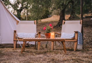 Zona relax con due sedie, tavolino, pianta e candela davanti a una tenda Bell in Italia.