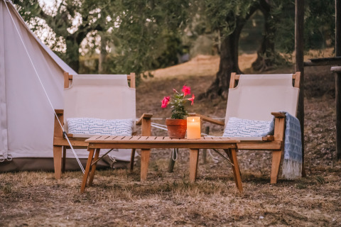 Zona relax con due sedie, tavolino, pianta e candela davanti a una tenda Bell in Italia.
