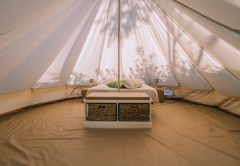 Intérieur de la tente Bell à l’Agriturismo Angeli Sognanti en Italie, avec lit et paniers dessous.