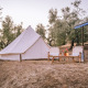 Tienda tipo Bell instalada entre olivos, con cómodas sillas y una mesa bajo un dosel sombreado.