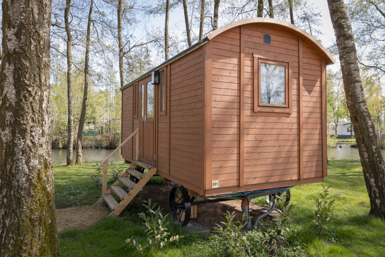 Cabaña Pipowagen de madera con escaleras en un bosque, cerca de un estanque tranquilo.