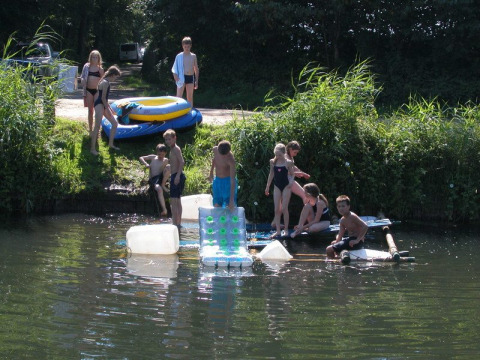 Children playing on a homemade raft in the water at Feather Down Het Wesselink in Salland, Overijssel, Netherlands.