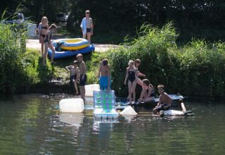 Kinder spielen auf einem selbstgebauten Floß am Wasser im Feather Down Het Wesselink in Salland, Overijssel.
