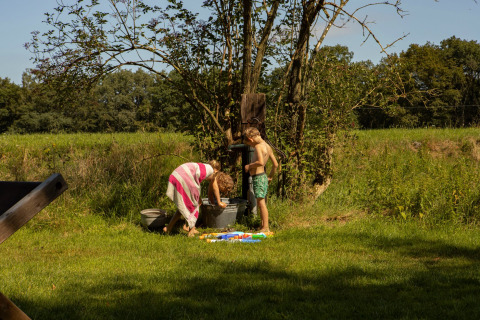 Zwei Kinder spielen an einer Wasserpumpe im Grünen im Feather Down Het Wesselink in Salland, Niederlande.