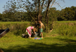 Zwei Kinder spielen an einer Wasserpumpe im Grünen im Feather Down Het Wesselink in Salland, Niederlande.