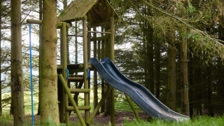 Legeplads med rutchebane og træstruktur blandt træerne på Feather Down Hidcote Manor Farm, West Midlands.