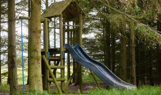 Legeplads med rutchebane og træstruktur blandt træerne på Feather Down Hidcote Manor Farm, West Midlands.