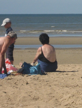 Gezin geniet op het zandstrand bij een vakantiedomein dat glamping-accommodaties aanbiedt.