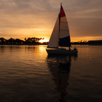 Zeilboot op kalm water bij zonsondergang rond Blandford Forum, Zuidwest-Engeland, bomen als silhouet.