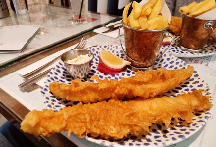 En lækker tallerken fish and chips serveret med citron, tartarsauce og pommes frites i en spand på restaurant.