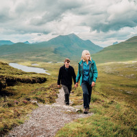 To personer vandrer på en sti omgivet af frodige bakker nær Jedburgh, Nordvestengland, under overskyet himmel.