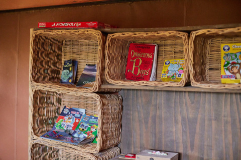 Étagères en osier avec livres et jeux d’enfants, dont Monopoly, au parc Feather Down Chesters, Angleterre.