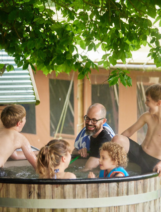 Familie nyder varmt bad under et træ hos Feather Down Chesters feriepark i Nordvestlige England.