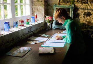Jongen schrijft aan een rustieke tafel met conserven op de vensterbank bij Feather Down Chesters, Noordwest-Engeland.