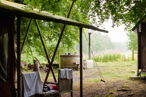 Gezicht op een buitencamping bij Feather Down Chesters met houten hut en mensen in een warm bad.