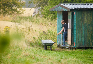 Ein Junge lädt Holz aus einem grünen Schuppen in eine Schubkarre bei Feather Down Chesters, Nordwestengland.