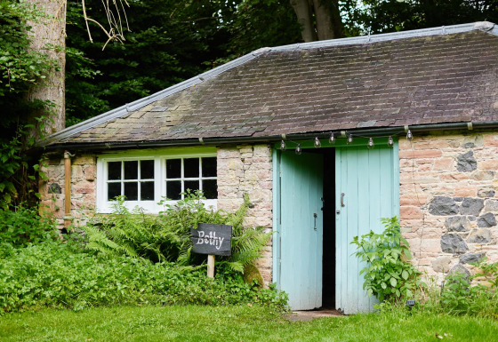 Knus stenen huisje met mintgroene deuren, een 'Bothy'-bord, gelegen te midden van weelderig groen.